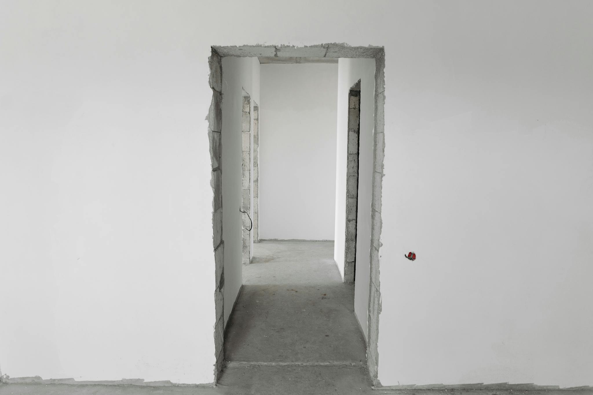 Interior view of a simple white corridor in an unfinished building, showing raw construction details.